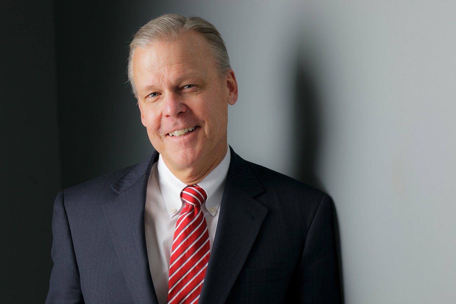Photo of Dean Daniel Gurskis in a suit and tie on a grey background.