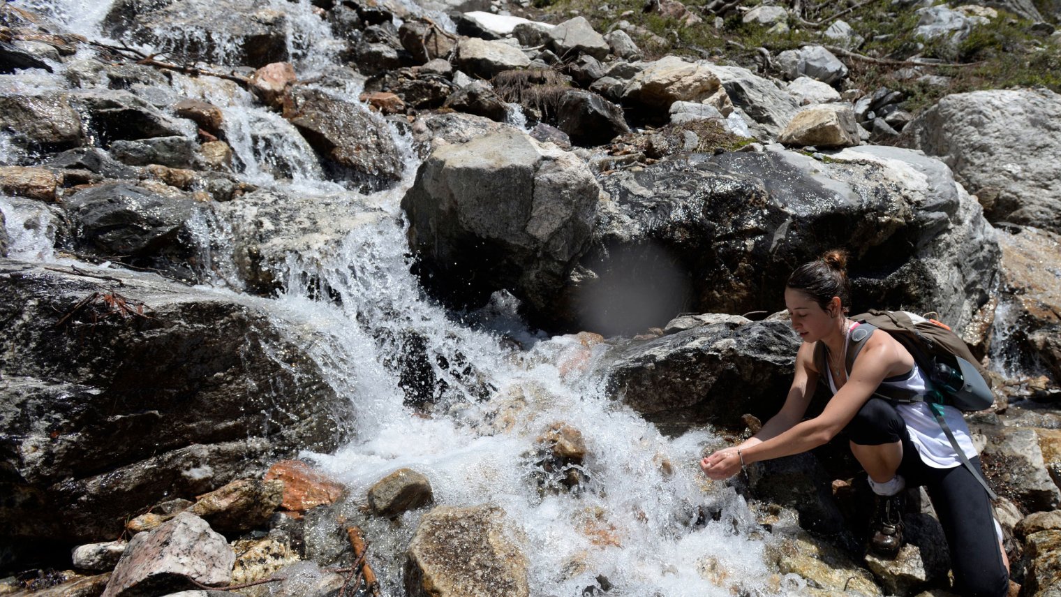 student on class hike getting water from a rushing stream