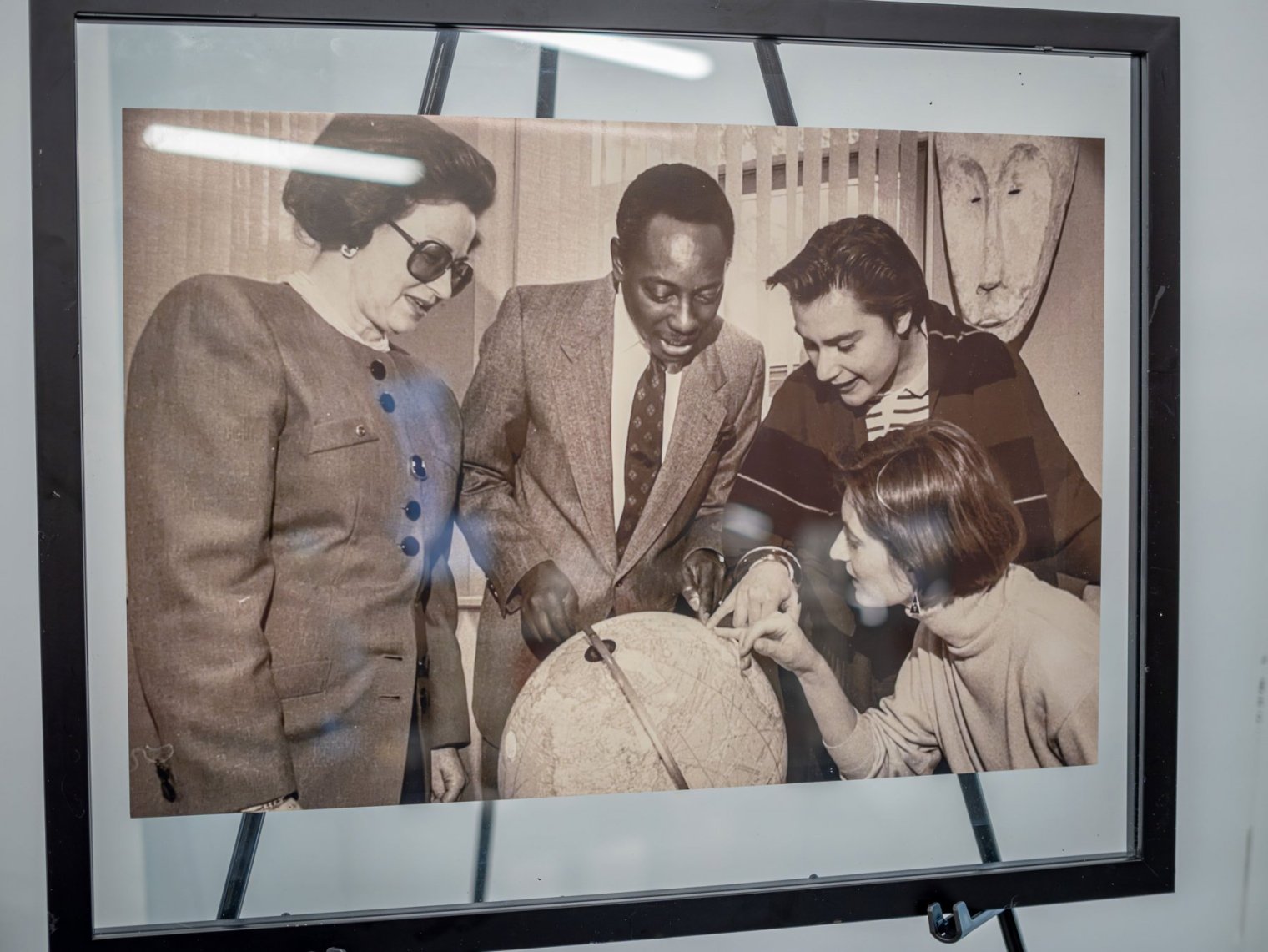 A framed black and white photo of four people standing around a globe