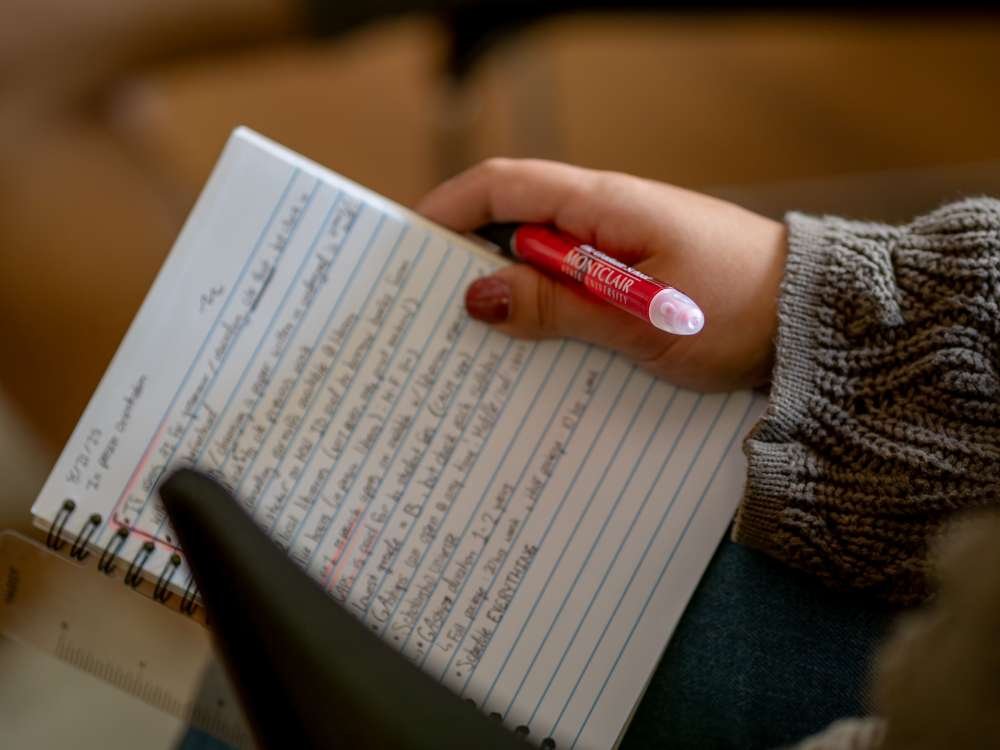A person holding a notebook filled with handwritten notes and a red pen.