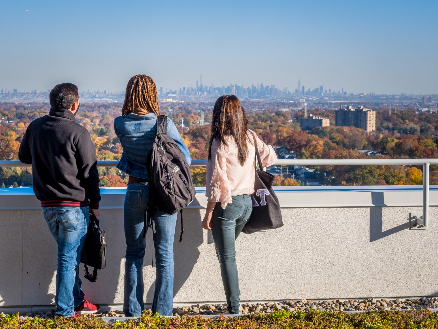Three people stand with backs to camera looking at New York City skyline from Montclair's campus