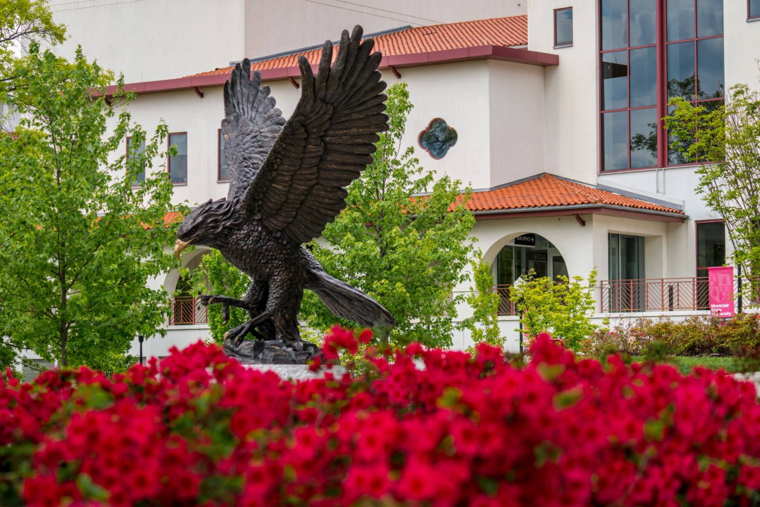 A row of red flowers sits in front of a large, bronze statuue of a Red Hawk