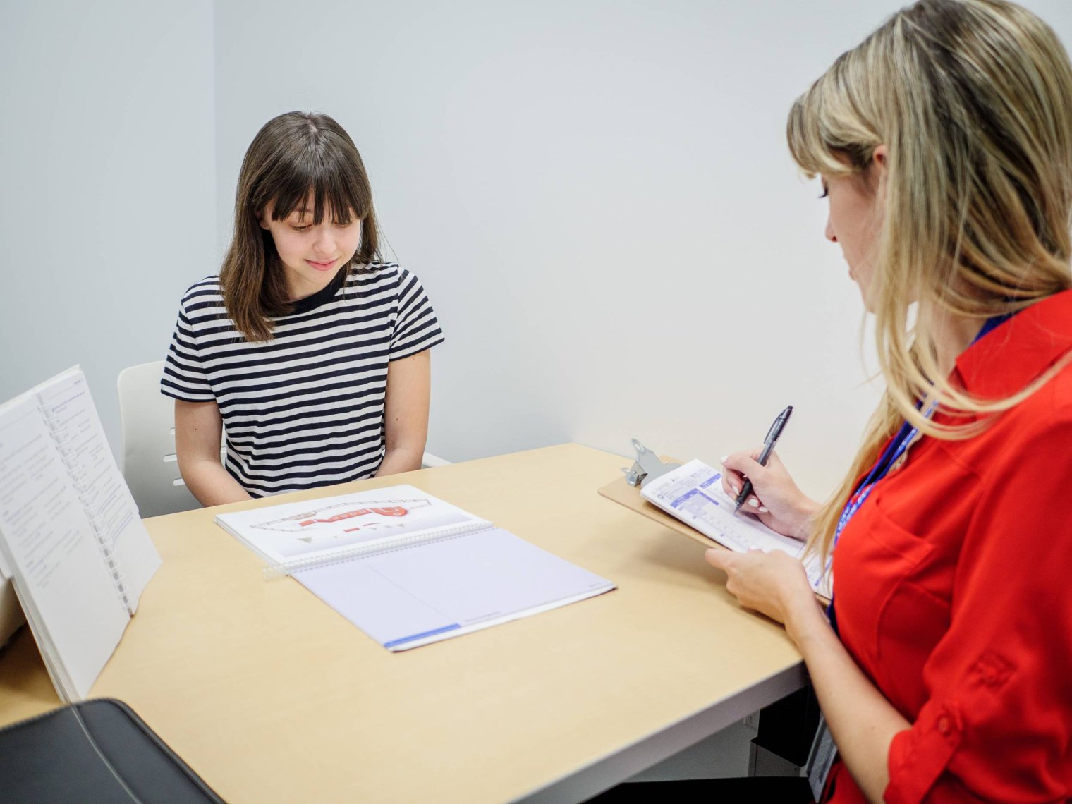A woman takes notes as a younger woman studies a paper on a table