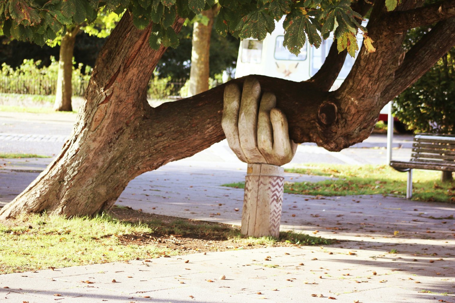 A carved hand sculpture seemingly support a heavy tree limb in a park setting