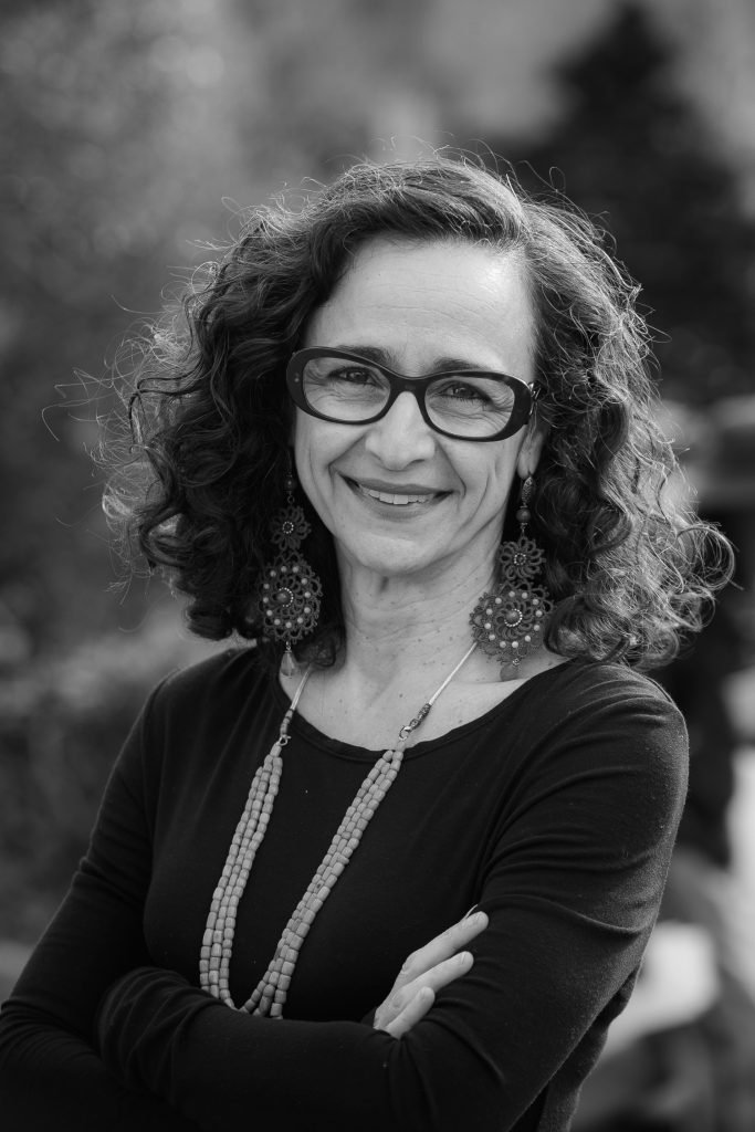 A black and white headshot of a woman posing with her arms crossed outside