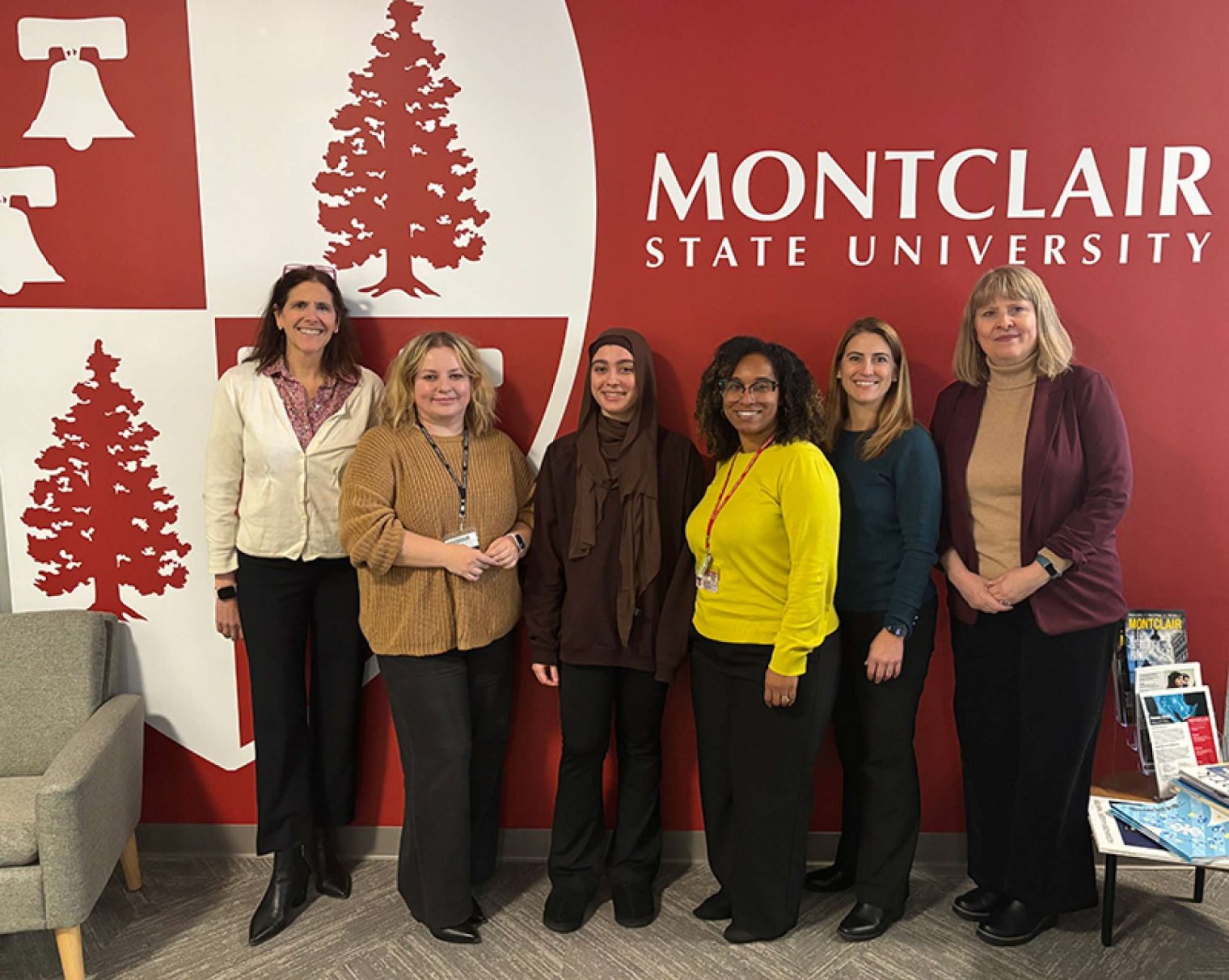 A group of six people pose in font of a Montclair State University logo painted on a wall