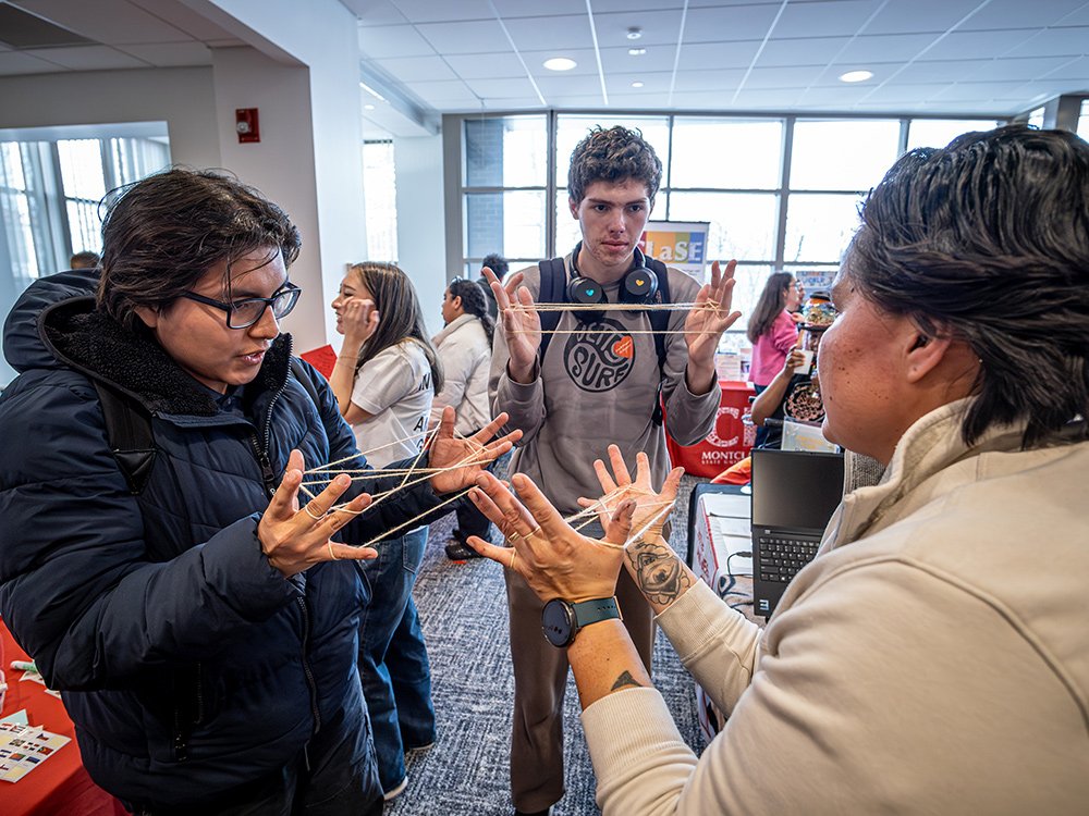 A college professor demonstrates a cat's cradle to two students who follow along with their own string