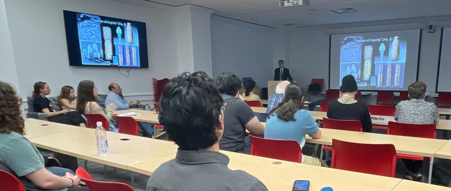 A classroom full of college students listens to a man lecture from a podium