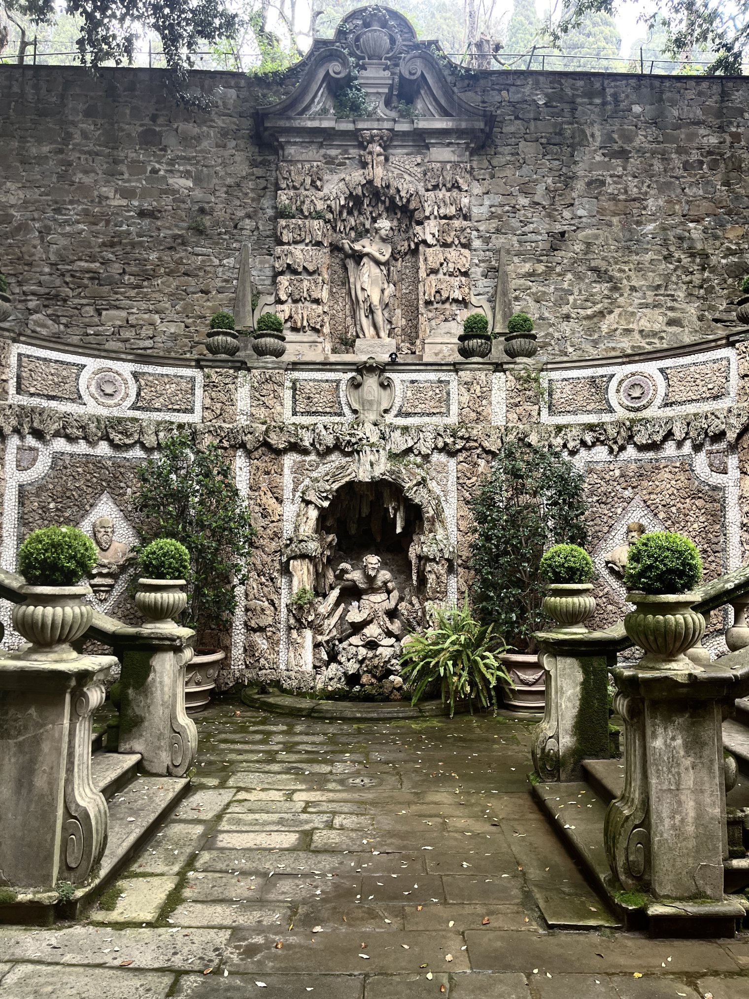 Garden feature at Villa Le Balze with stone statues set into a stone wall and symmetrical staircases leading to a lower terrace