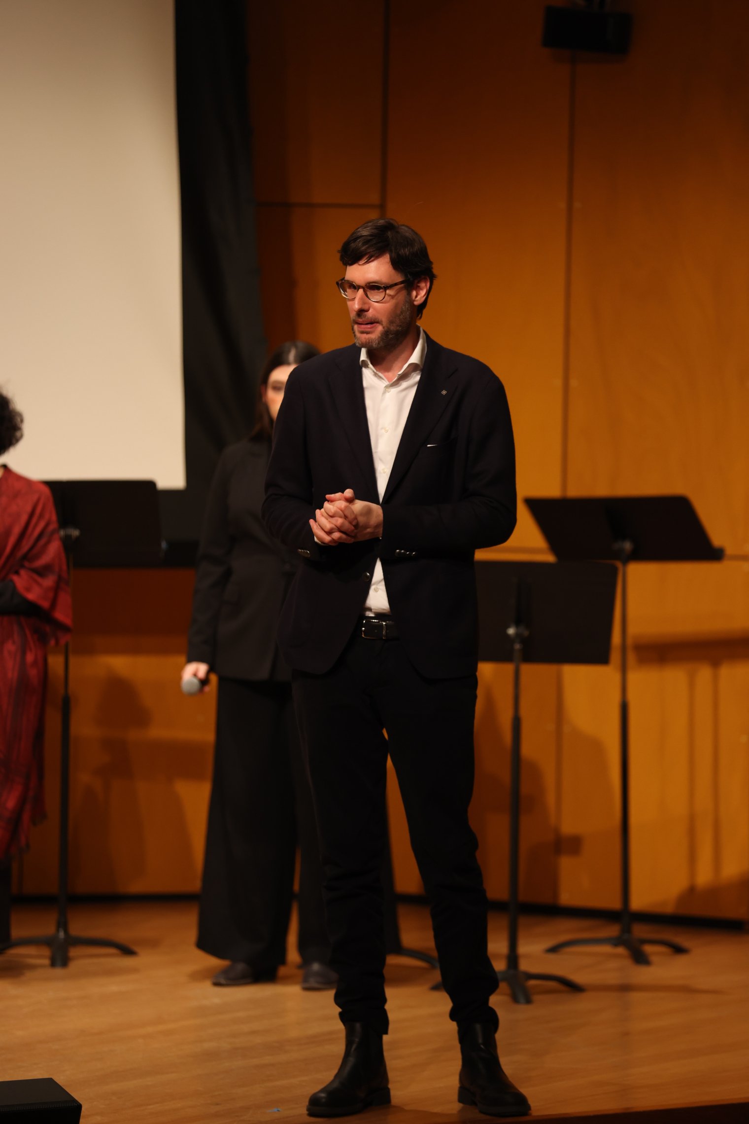 Maestro standing on stage in a suit addressing the audience