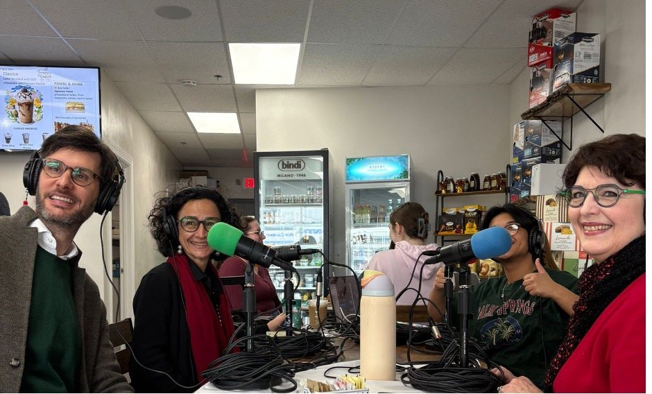 A group of four adults sit at small table with two microphones for an interview