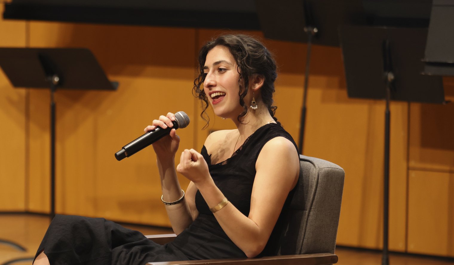 A college students sits in a chair on stage and speaks to the audience with a microphone