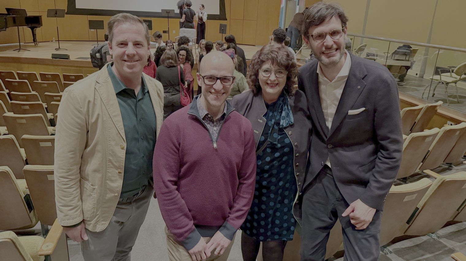 A group of four adults pose in a line inside an auditorium