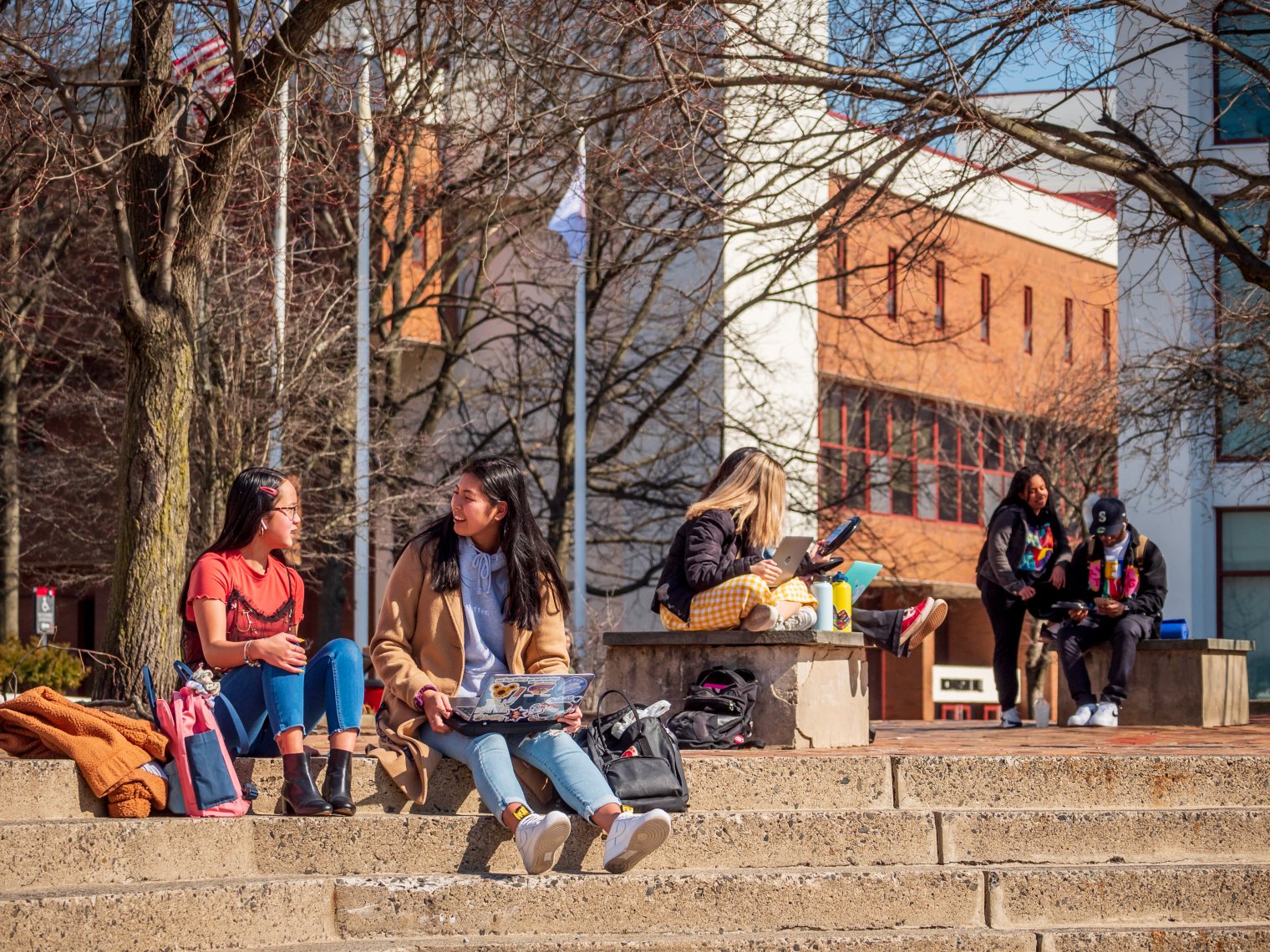 Two students in the foreground sitting on the steps near Richardson, with other students seated on benches nearby