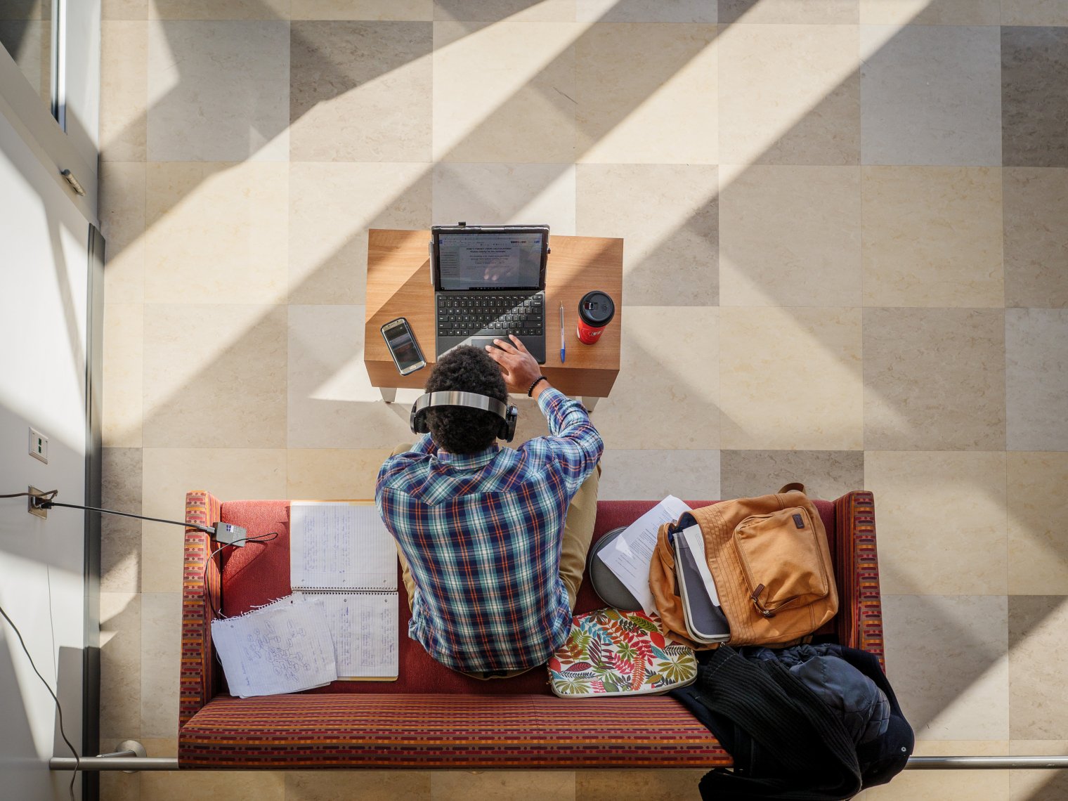 An overhead shot of a student working at a laptop seated on a couch