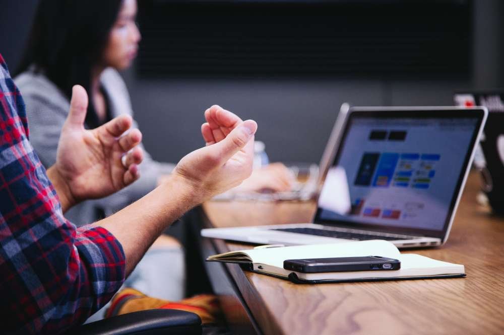 Person gesturing with hands near a laptop and notebook during a class.