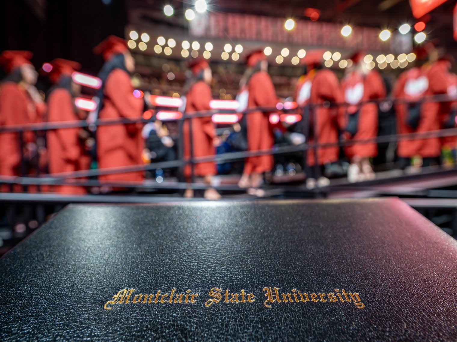Diploma with graduates lined up on stage in background