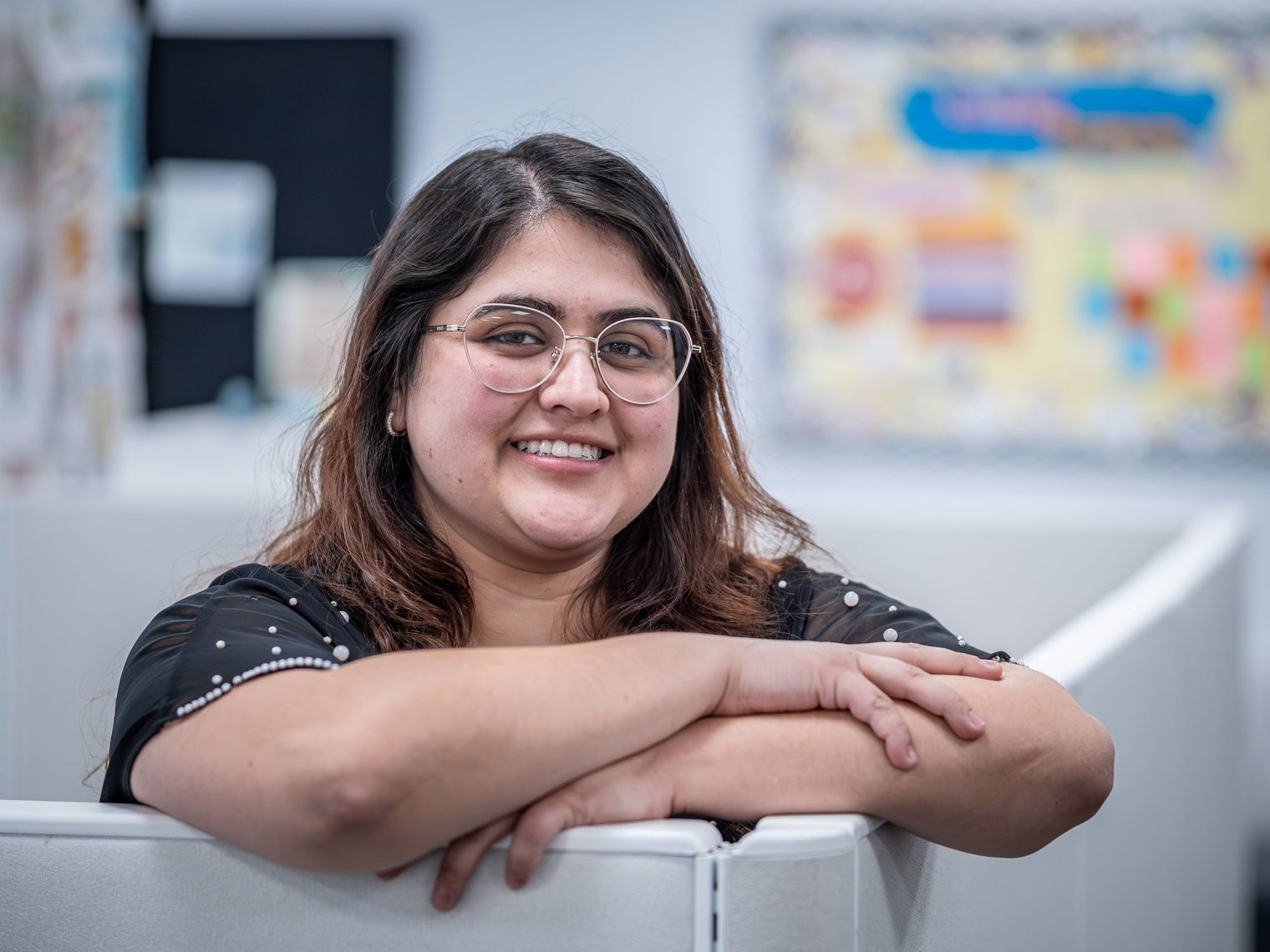 Isabella Gonzales smiling with her arms crossed over a cubicle.