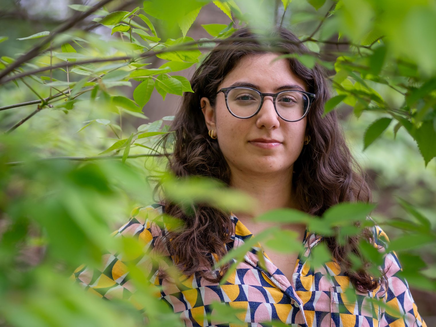 Tia Atieh between some green leaves with glasses on.
