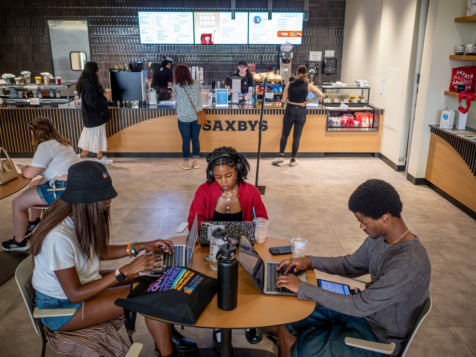 Three students sitting at a table on laptops in a cafe. 