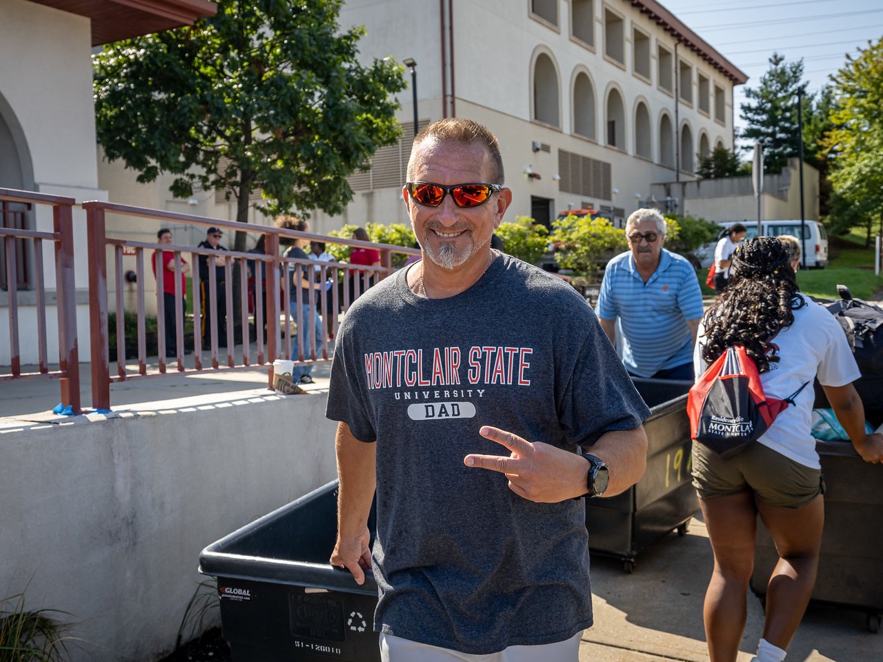 A man in a Montclair State Dad tshirt holding a peace sign with his fingers 