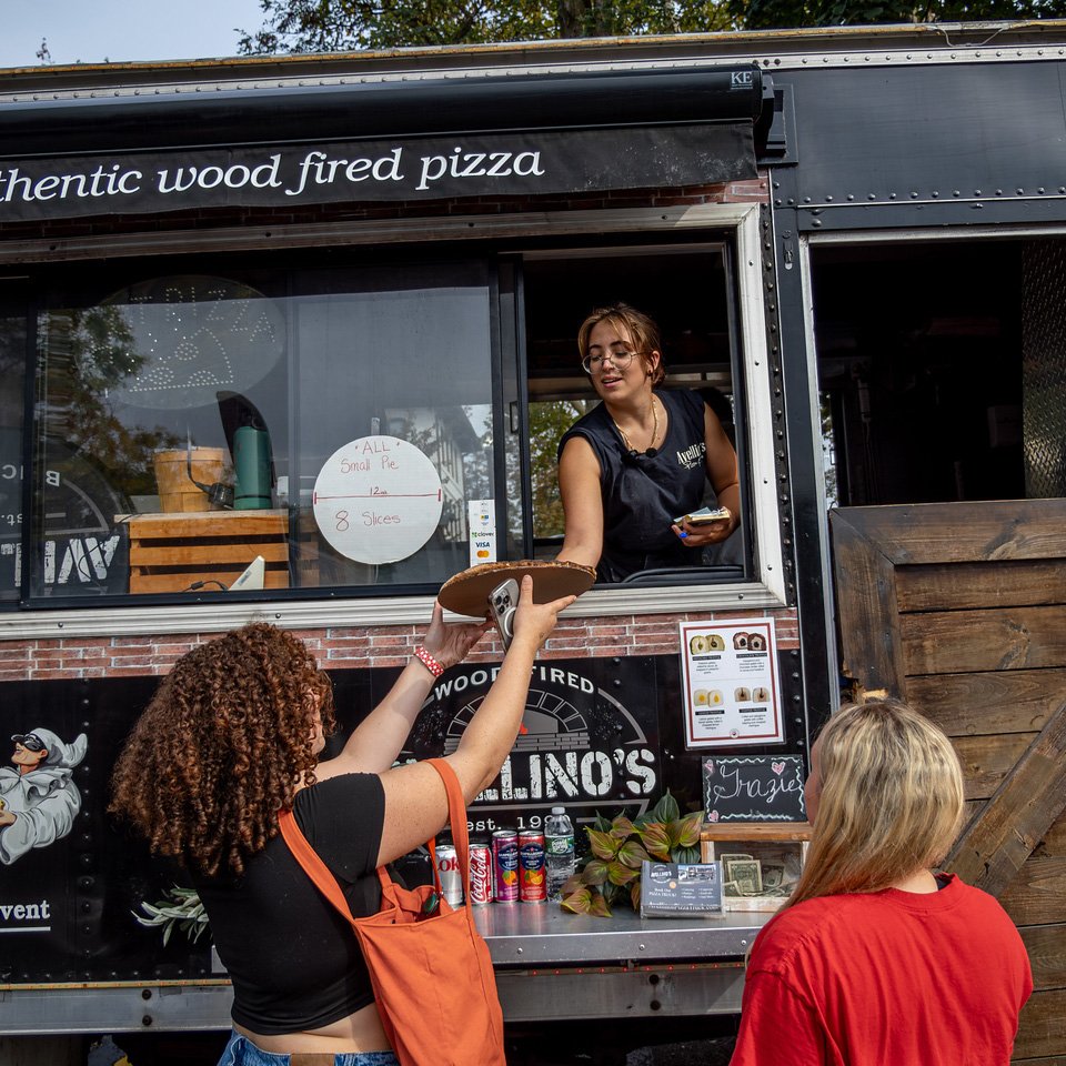 A pizza being handed from a food truck to a woman. 