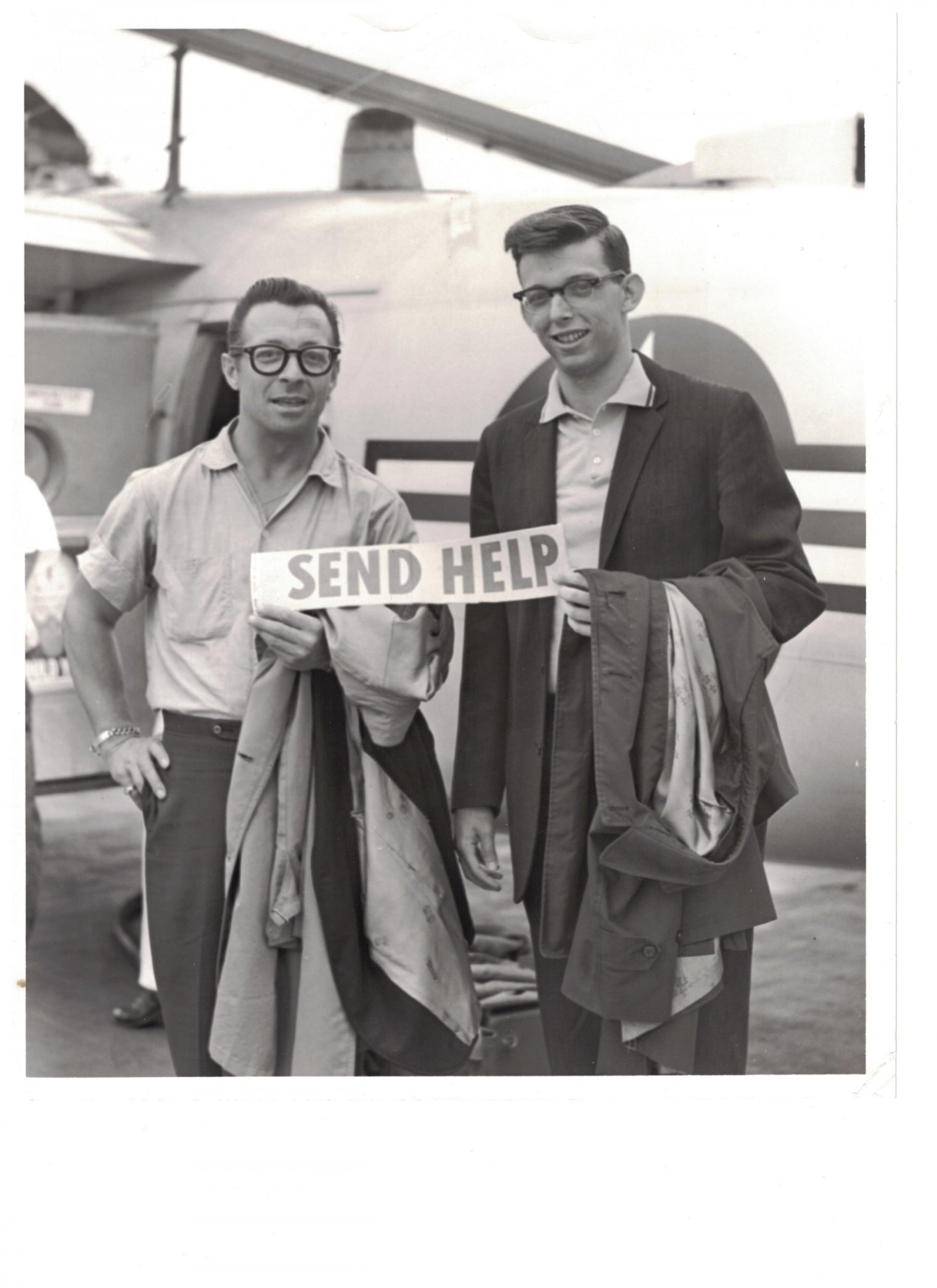 Black and white photograph of two adult men standing in front of an airplane