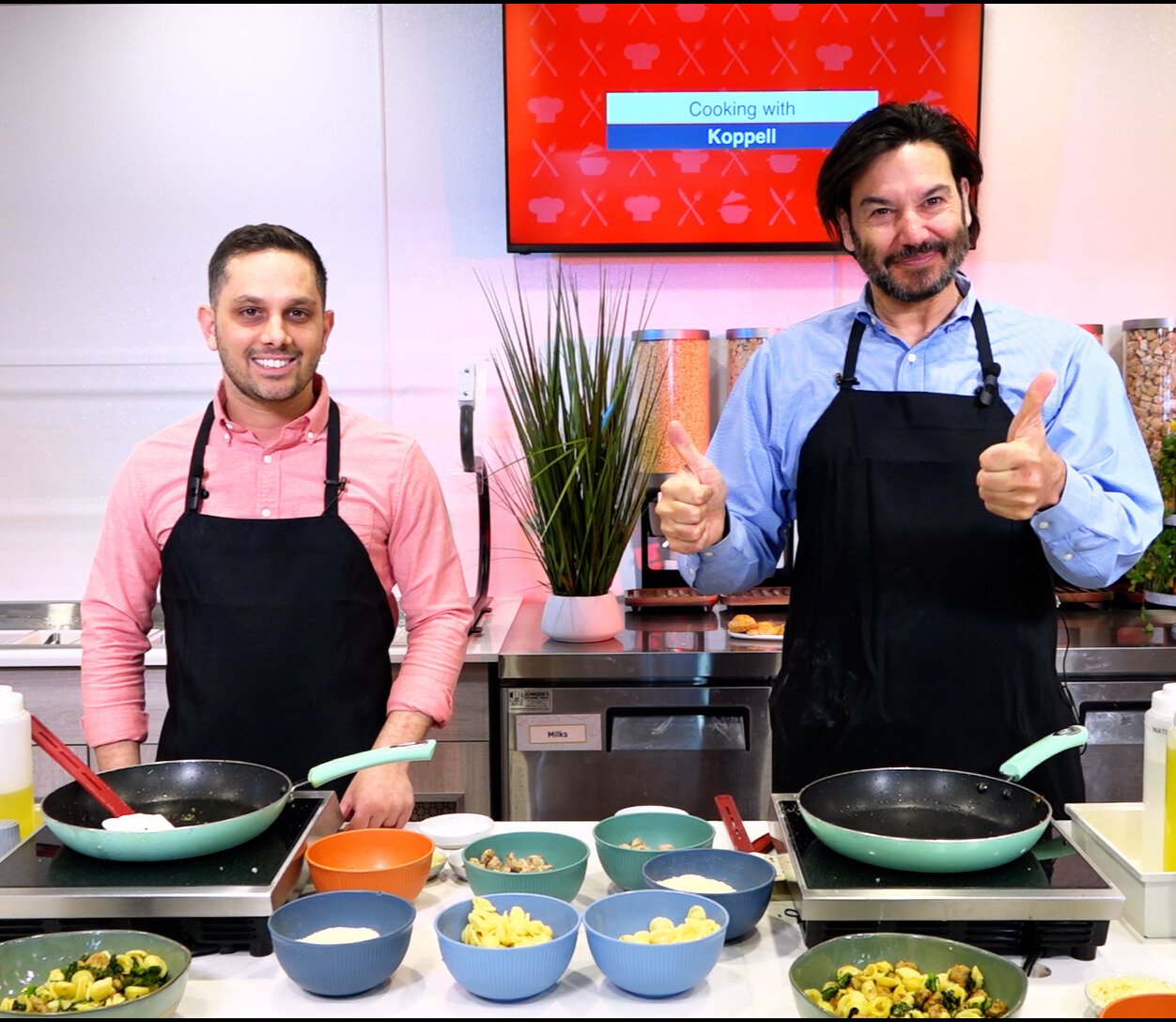 Antonio on left and President on right smiling for a photo with their black aprons on and food prepped on the table in front of them.