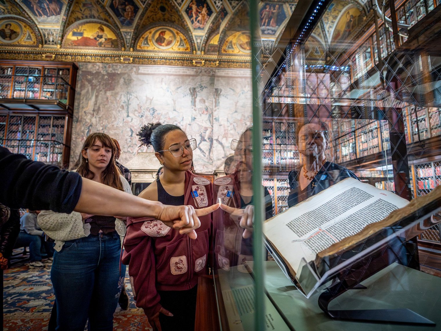 A group of college students looks at an ornate book behind glass as a docent points at it