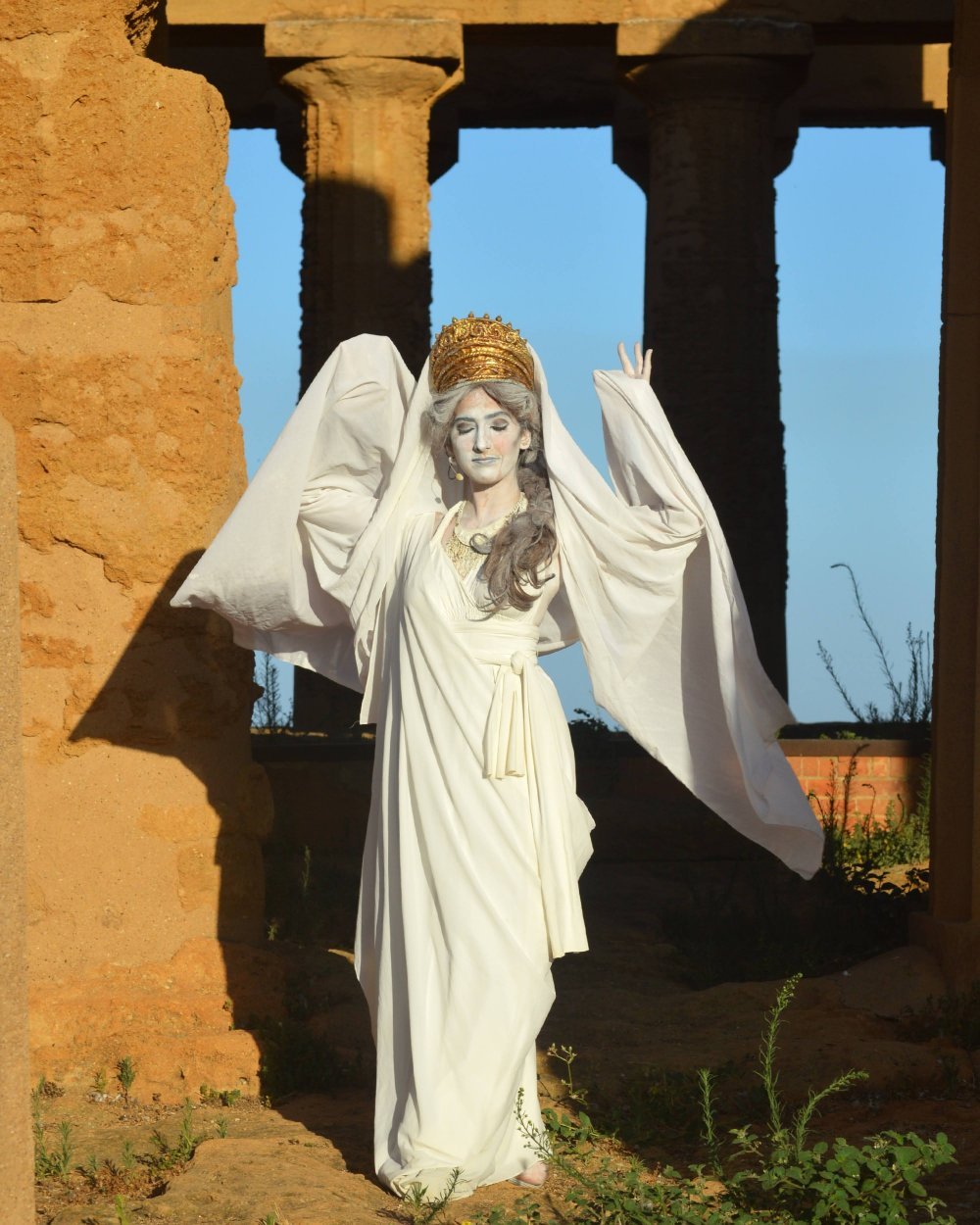 A woman in an ancient Greek costume poses in front of an ancient ruin outdoors