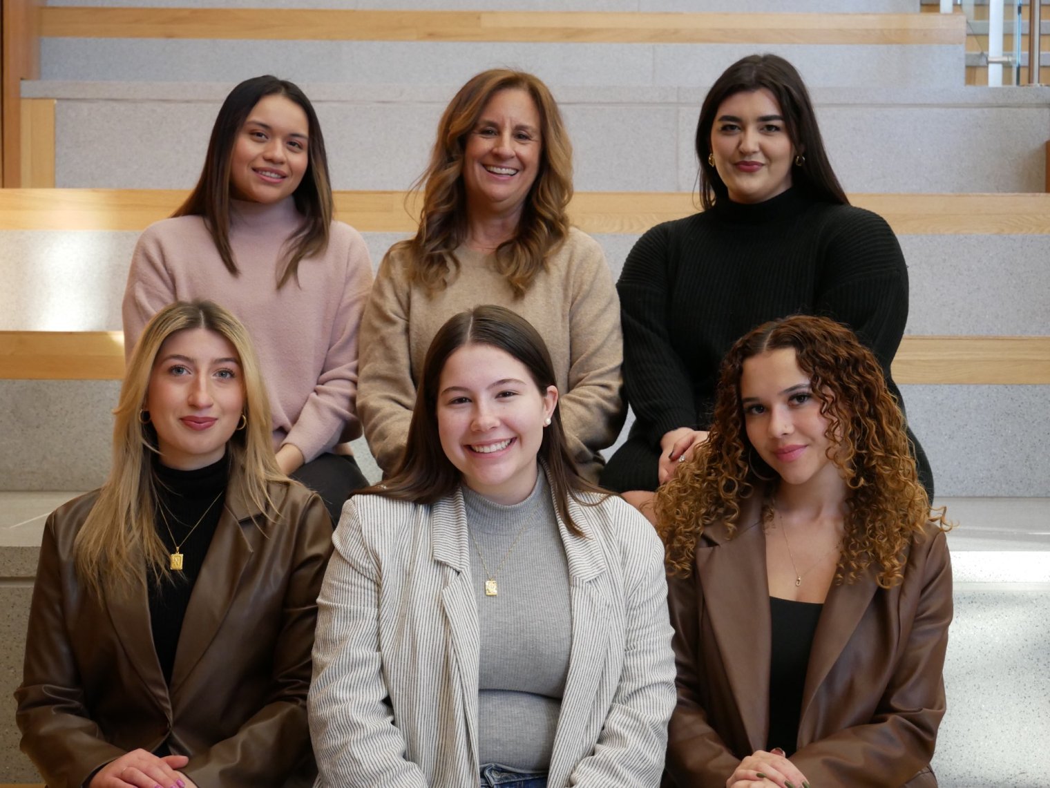 A team of six students and faculty sitting in two rows, smiling and dressed 
