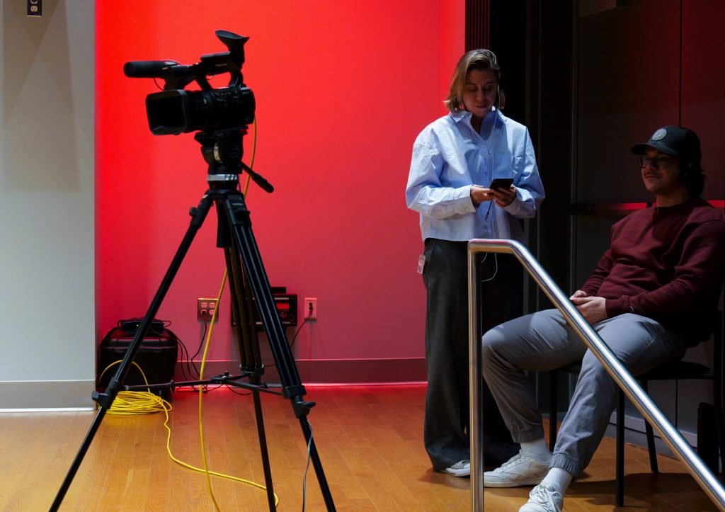 Camera setup on tripod on stage with red spotlight on the back wall.