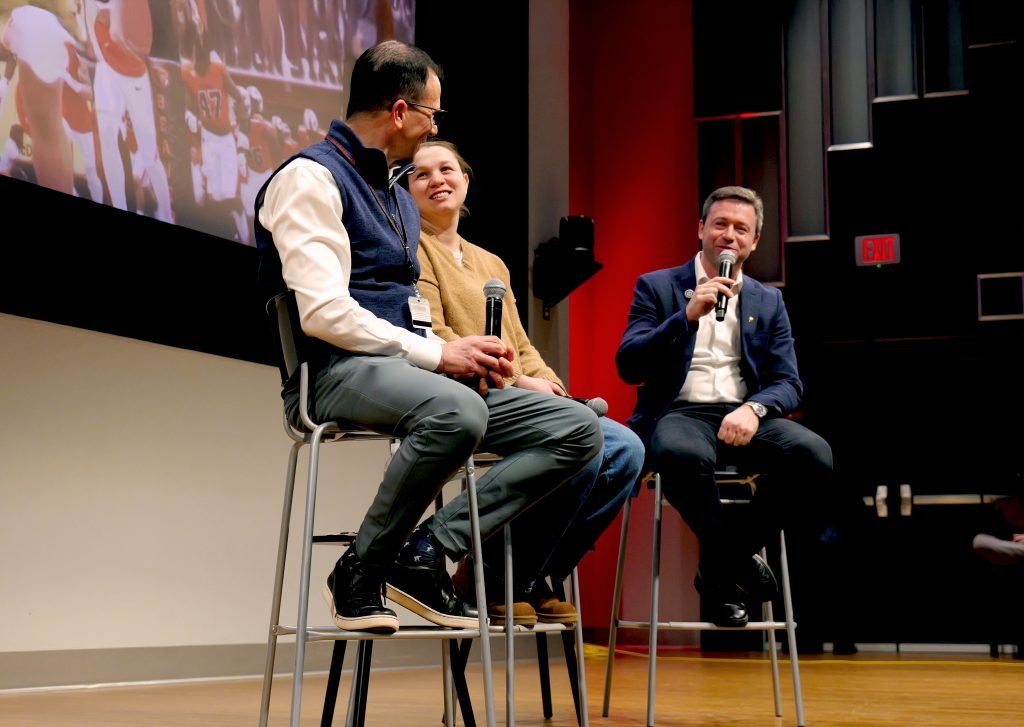 Three panelists on sitting on high-top stools on stage with mics in hand.
