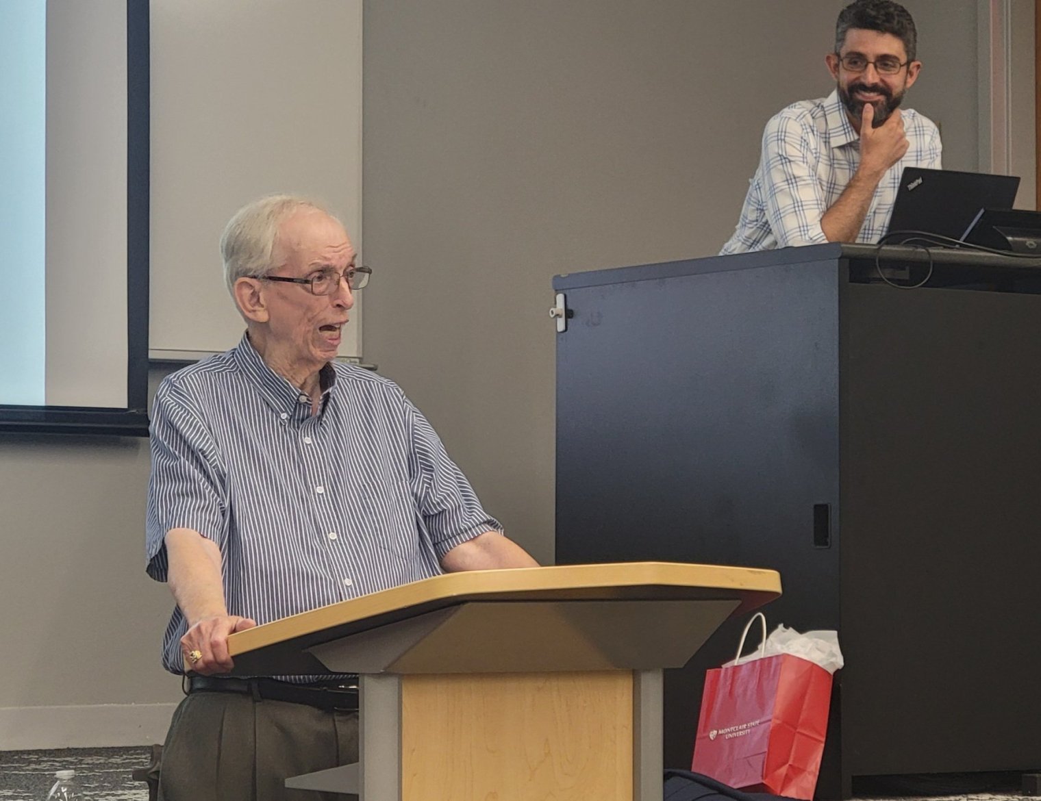 A old man stands at a podium and delivers a lecture to an audience