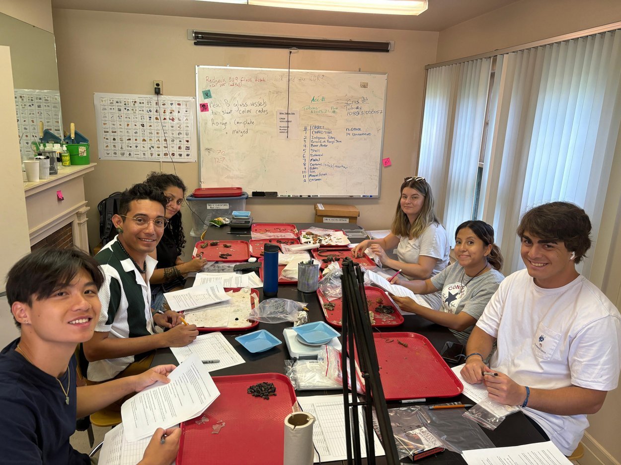 A group of college students sit around a table with artifacts and paperwork