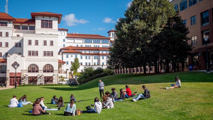 A college class sits on the lawn of a college campus