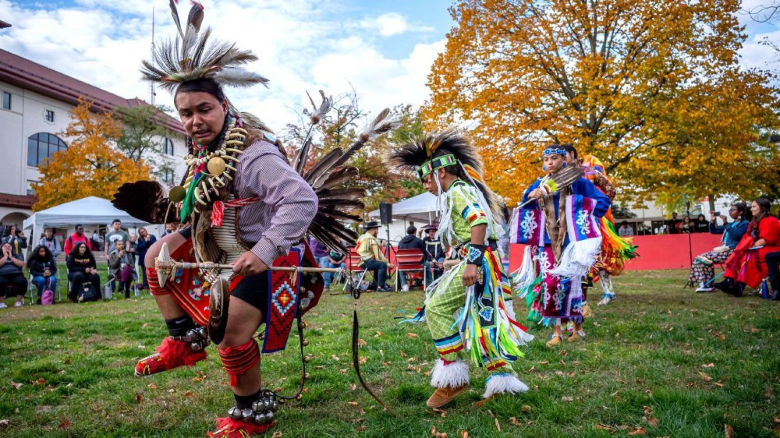 People wearing colorful Indigenous regalia perform a traditional dance at an outdoor cultural event