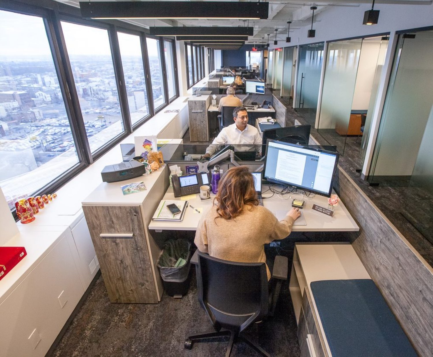 Interior of an office showing people sitting at desks beside a large window