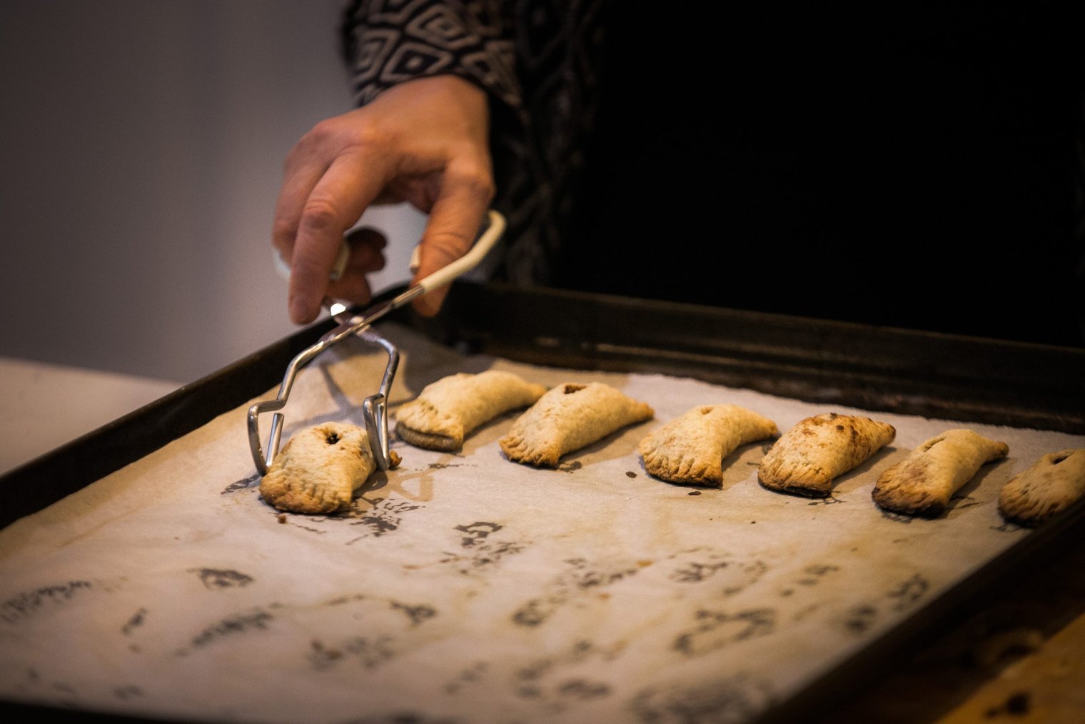 A hand holding tongs and picking a pastry off a cooking tray