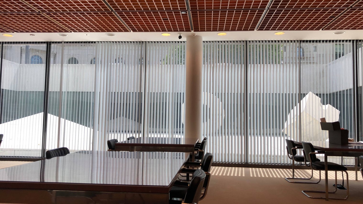 A room with a wall of windows and scattered empty tables and chairs