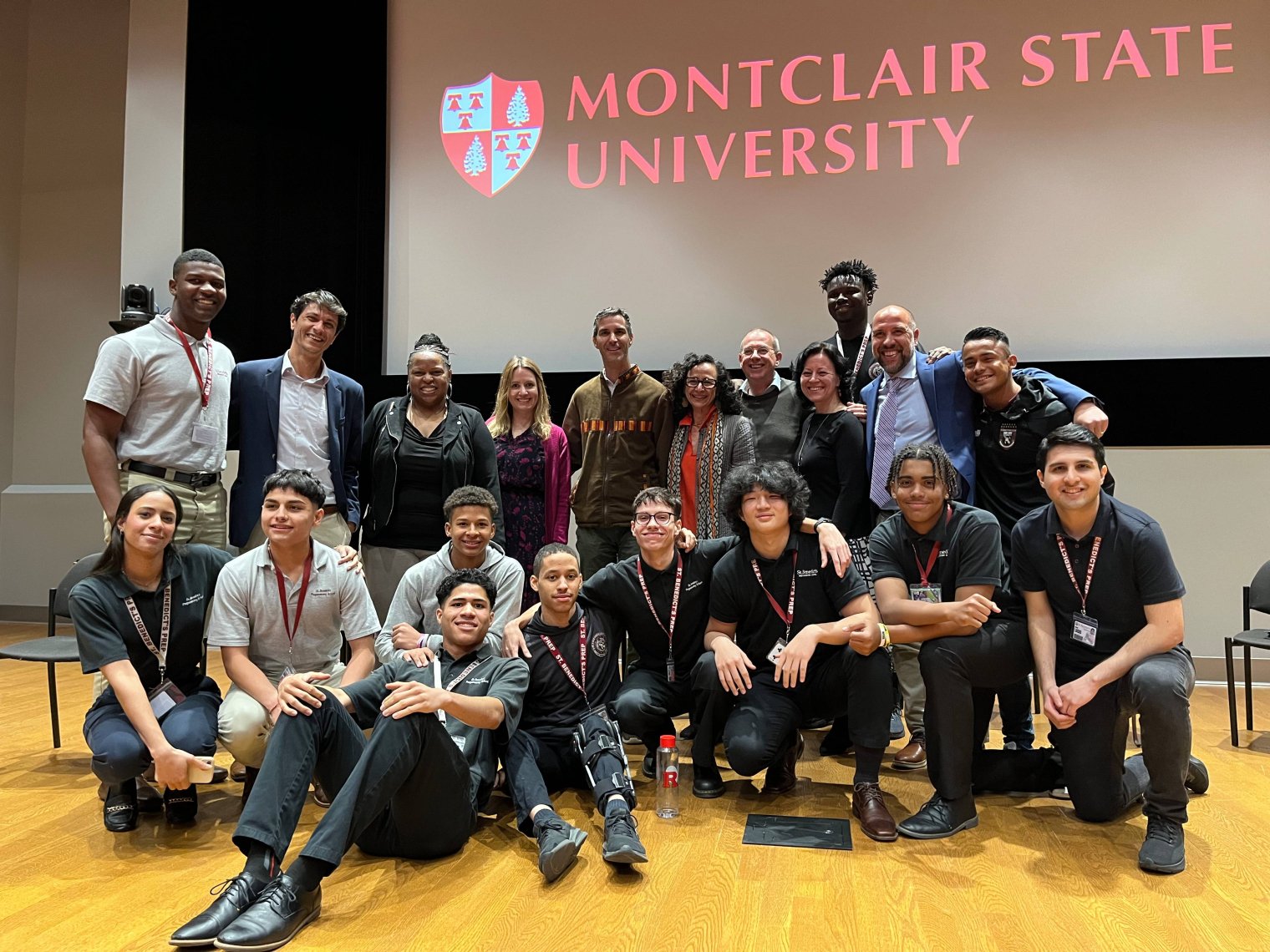 A group of college students pose in front of a projector screen bearing the words "Montclair State University"