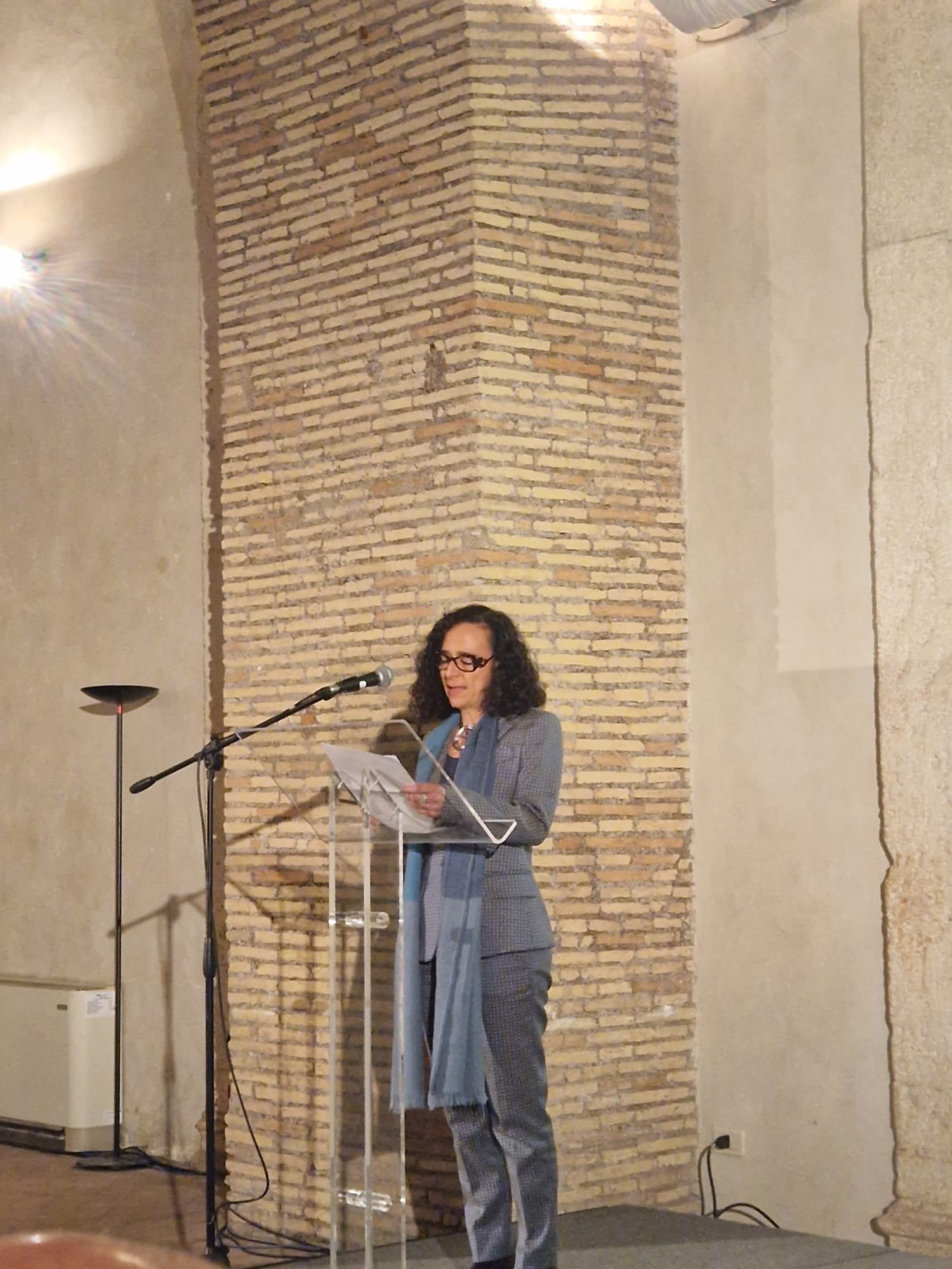 A woman stands indoors and delivers a lecture from a podium