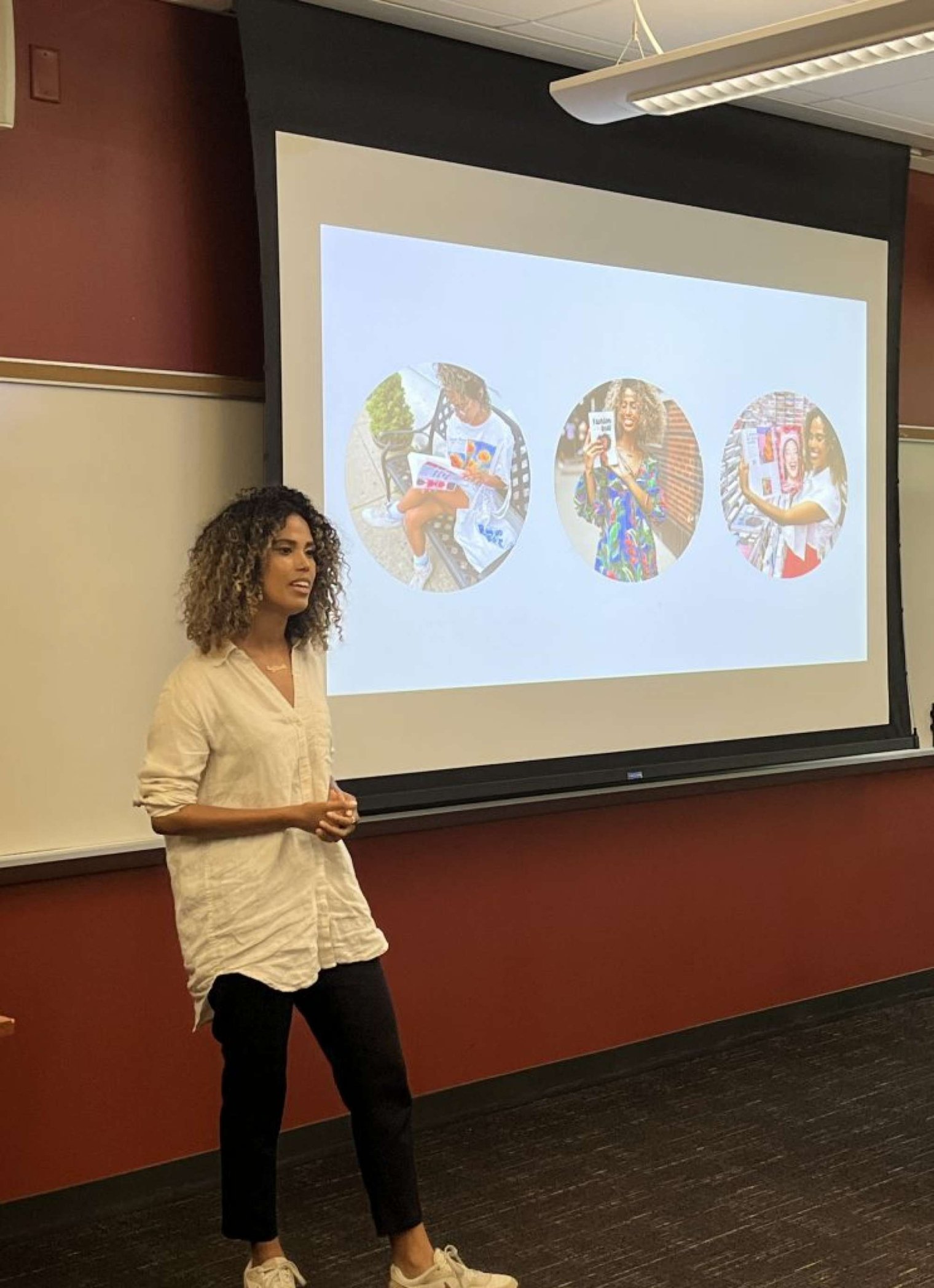 A woman stands beside a projector screen and addresses an audience