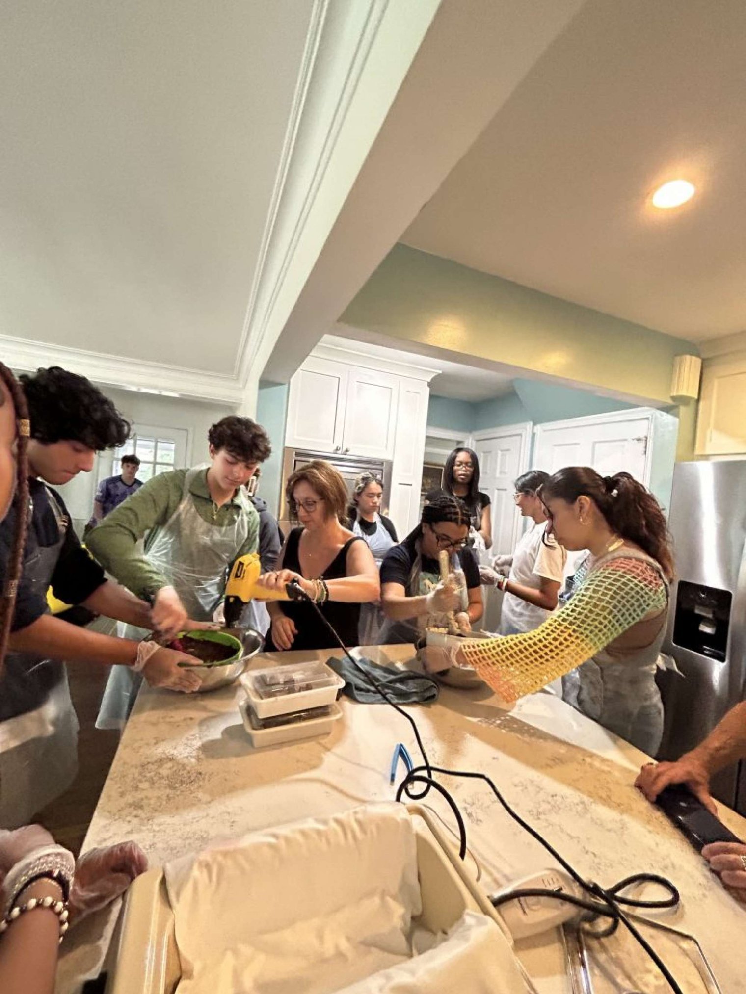 a group of college students stand around a kitchen counter and mix chocolate in a bowl