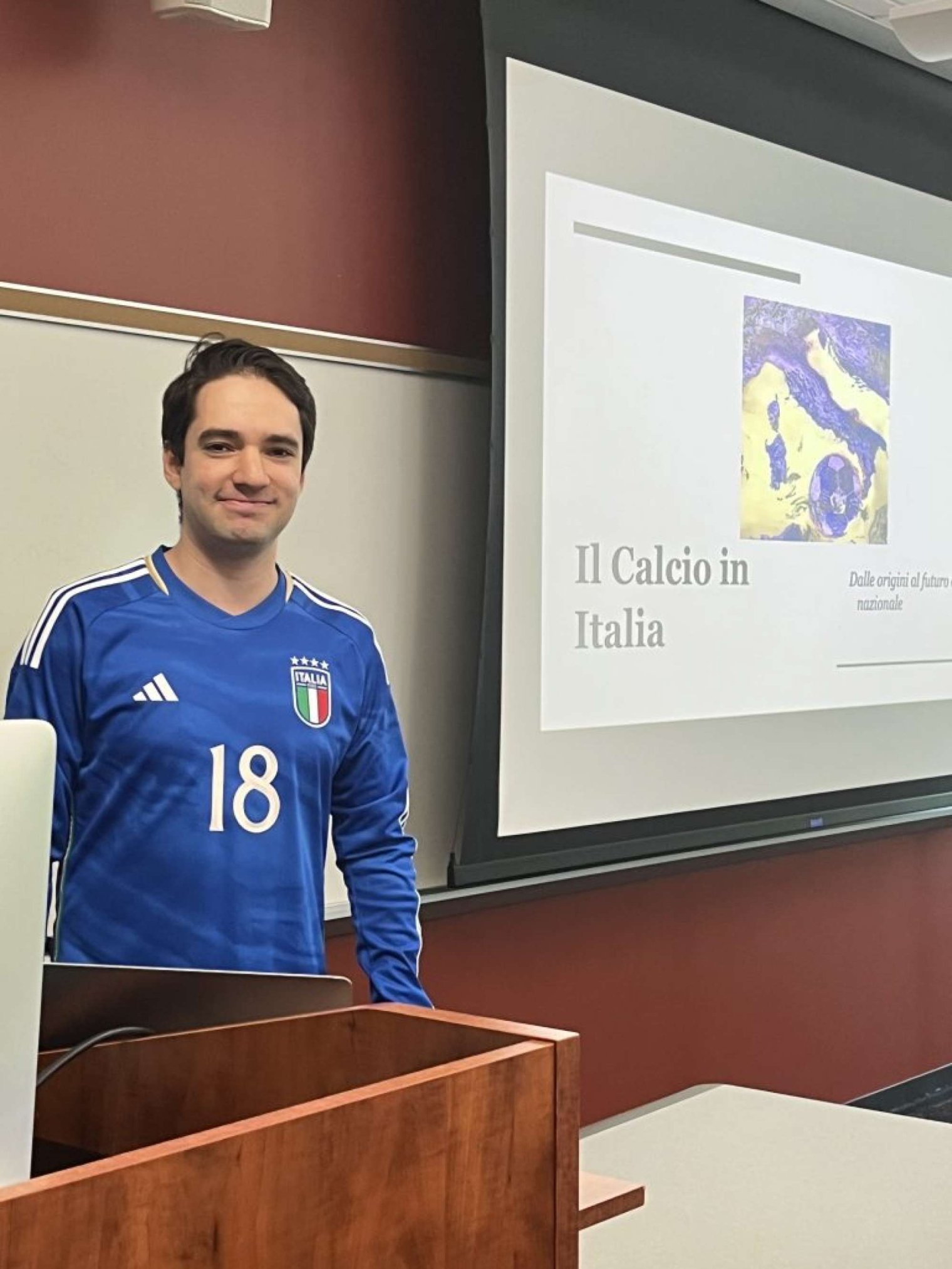 A man stands beside a projector screen and poses