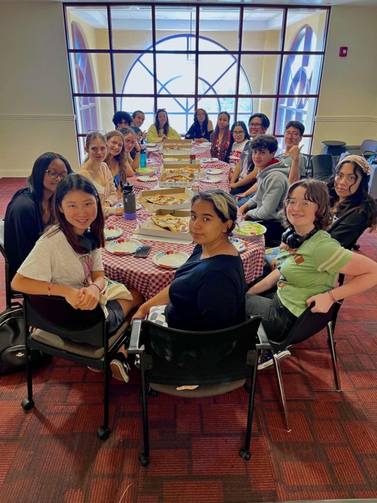 A group of college students sit around a table with pizzas 