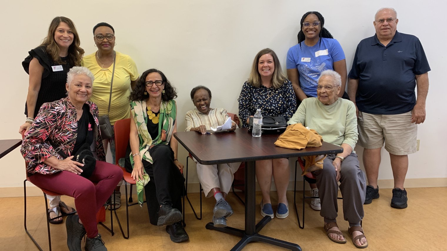 A group of people of diverse ages pose at a small table