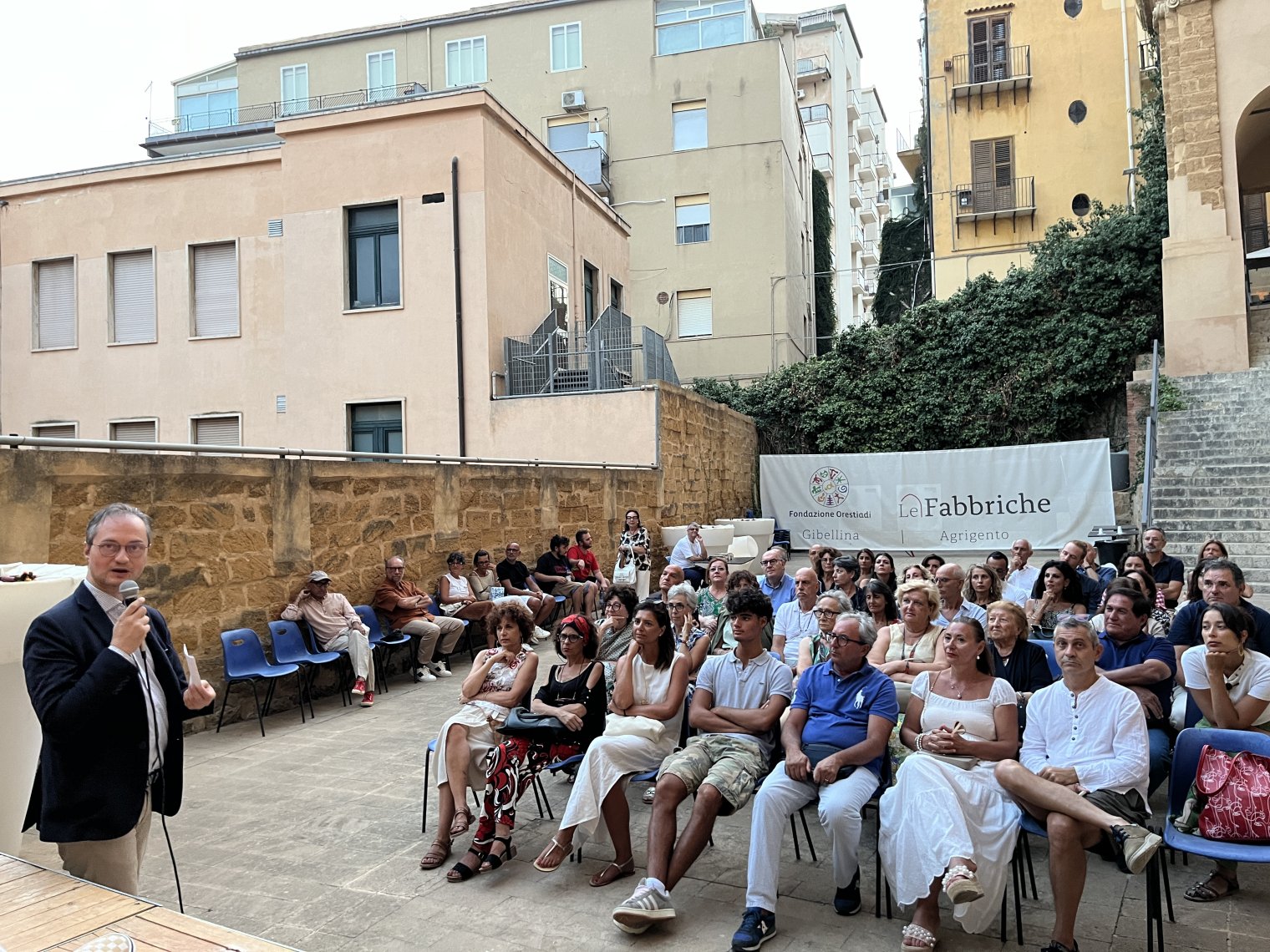 A crowd sits at an outdoor amphitheater as an MC talks into a microphone