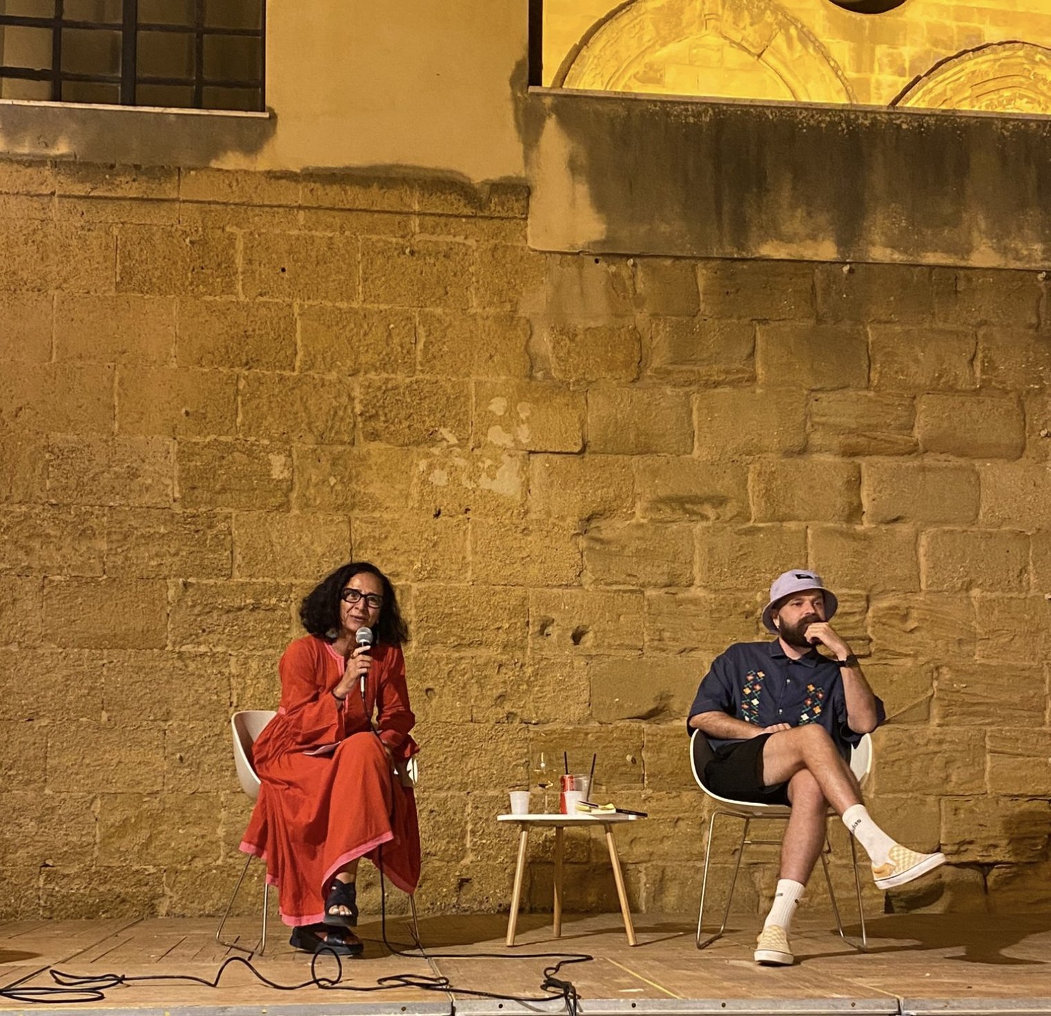 Two people sit in an outdoor auditorium and deliver a presentation