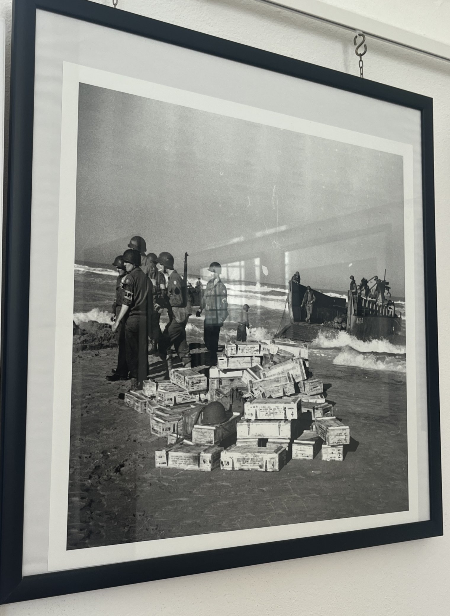 A framed black and white photo of U.S. WW2 soldiers stnading beside a pile of wooden boxes